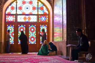 Un hombre lee el rezo en la mezquita mientras turistas se sacan foto en los vitrales.